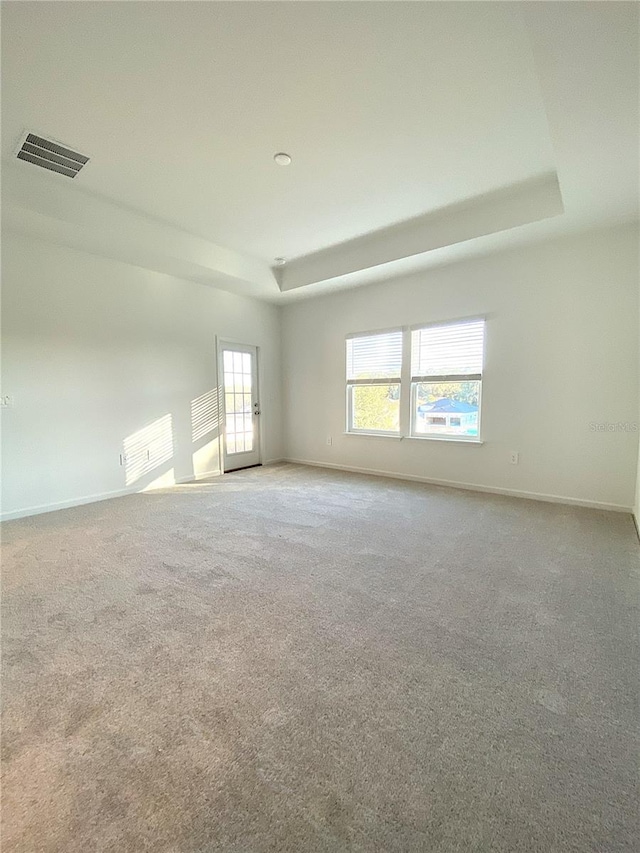 carpeted empty room featuring visible vents, a raised ceiling, and baseboards