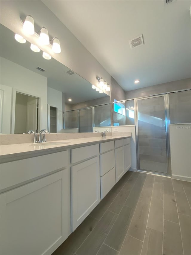 bathroom featuring double vanity, visible vents, a stall shower, and a sink