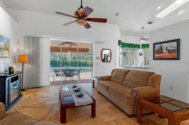 living room featuring a skylight, a ceiling fan, visible vents, and stone tile flooring