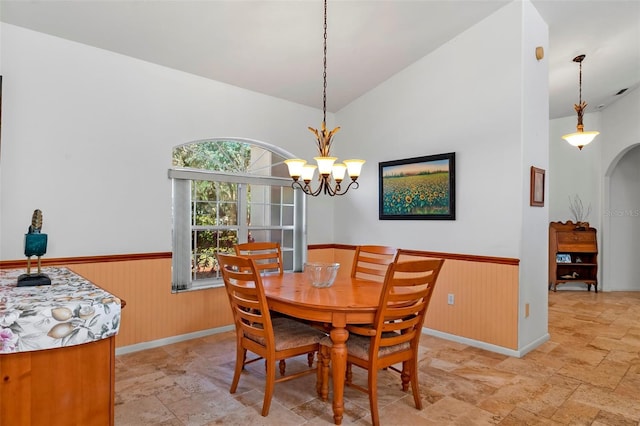 dining area with lofted ceiling, wooden walls, arched walkways, and a wainscoted wall