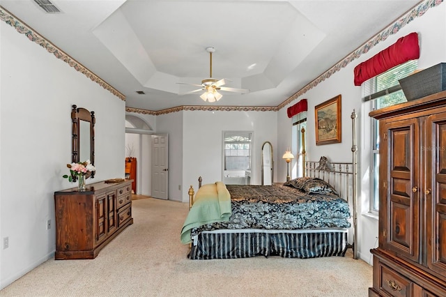 carpeted bedroom with baseboards, visible vents, ensuite bath, a tray ceiling, and ceiling fan