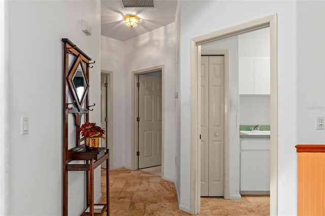 hallway with visible vents, stone finish flooring, baseboards, and a sink