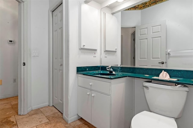 half bath with toilet, vanity, stone finish flooring, and baseboards