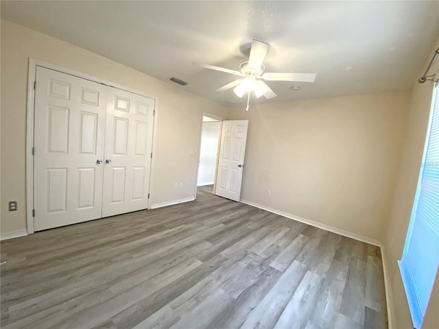 unfurnished bedroom with wood finished floors, visible vents, baseboards, ceiling fan, and a closet