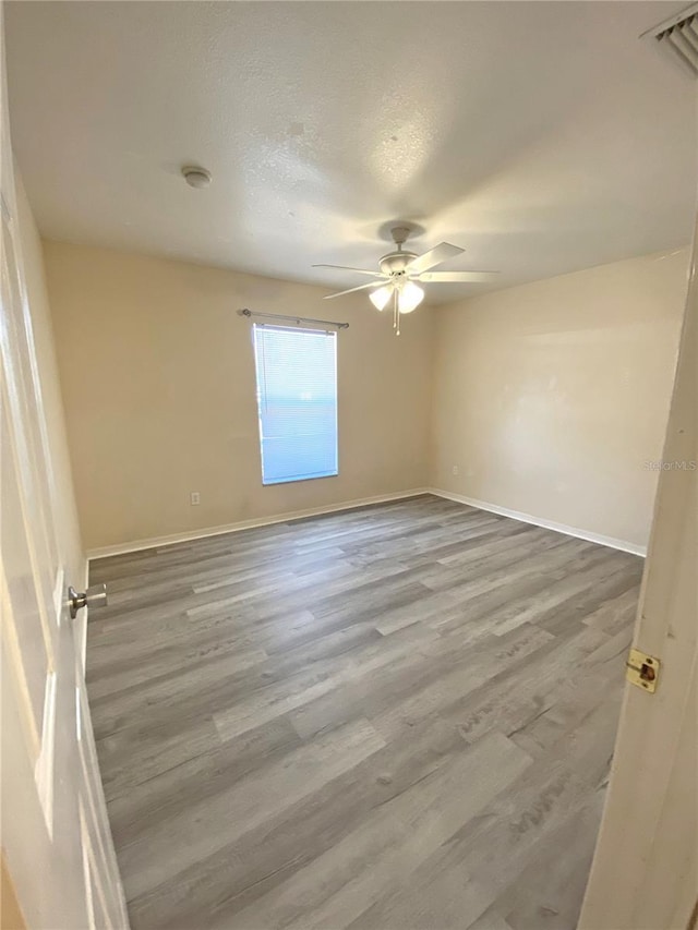 unfurnished room featuring baseboards, wood finished floors, visible vents, and ceiling fan