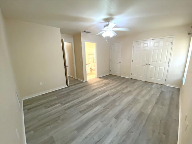 unfurnished bedroom with visible vents, ensuite bathroom, wood finished floors, baseboards, and ceiling fan