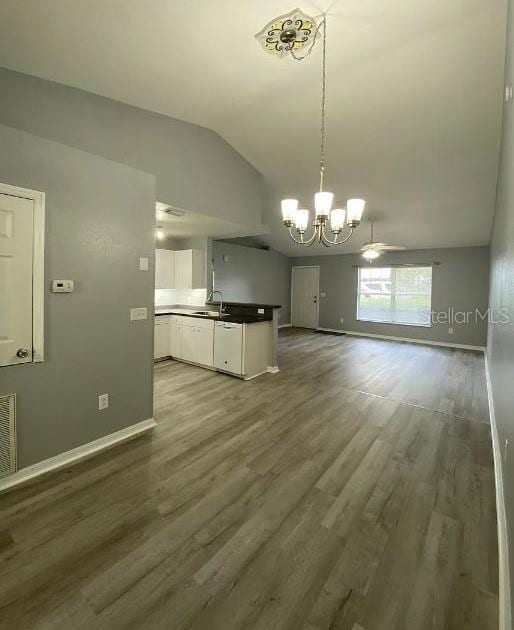 kitchen with wood finished floors, lofted ceiling, a sink, white cabinets, and open floor plan