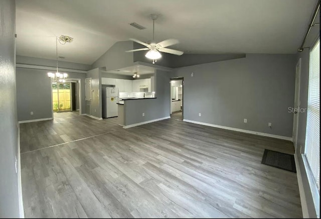 unfurnished living room with visible vents, ceiling fan with notable chandelier, wood finished floors, baseboards, and vaulted ceiling