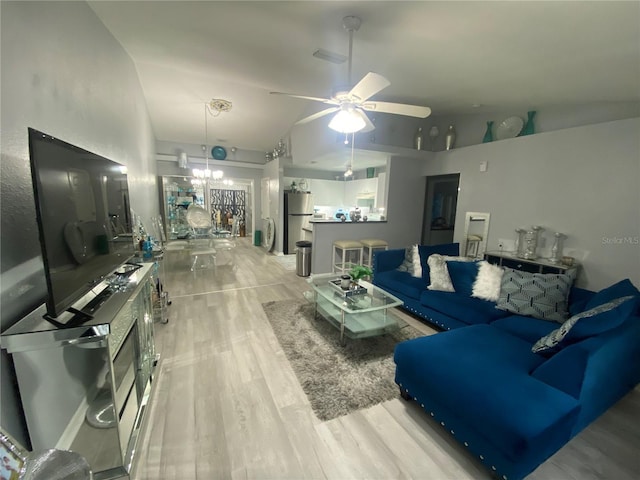 living area featuring ceiling fan with notable chandelier, visible vents, light wood-type flooring, and high vaulted ceiling