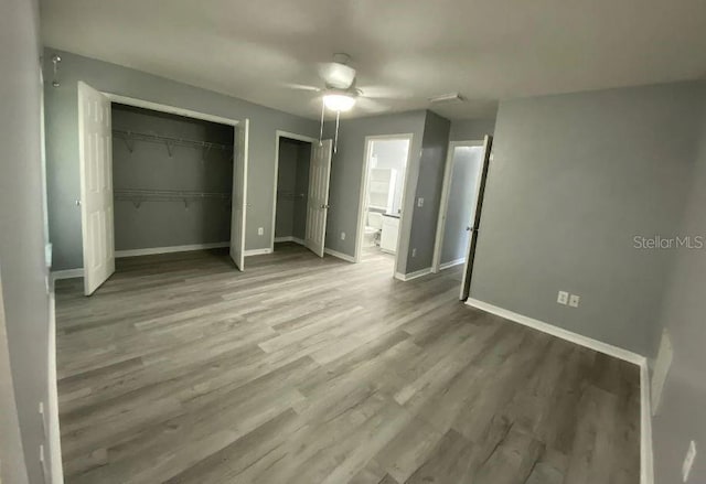 unfurnished bedroom featuring baseboards, ensuite bath, wood finished floors, and a ceiling fan