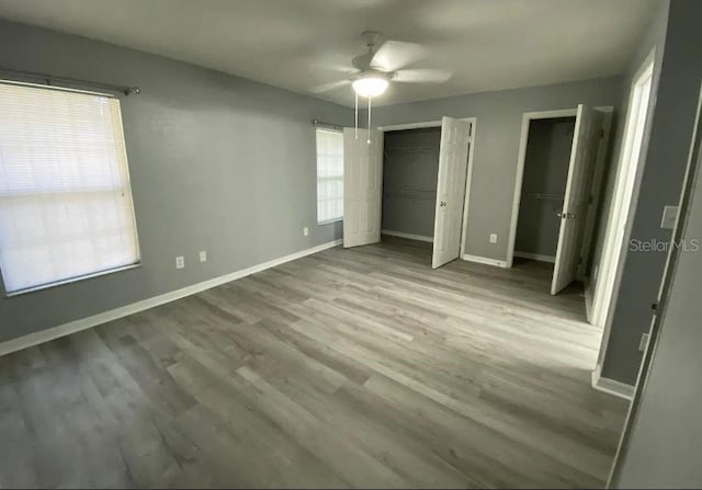 unfurnished bedroom with multiple closets, ceiling fan, baseboards, and wood finished floors