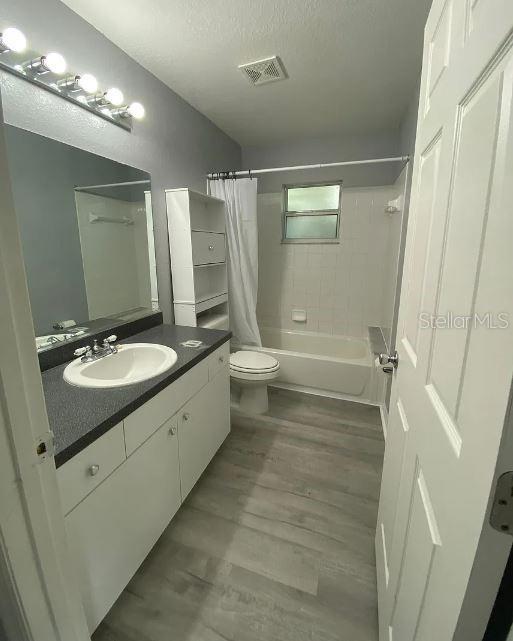 full bathroom with visible vents, a textured ceiling, wood finished floors, shower / tub combo, and vanity