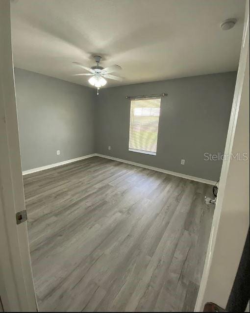 empty room with a ceiling fan, wood finished floors, and baseboards