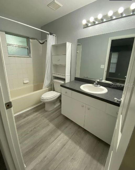 full bath with vanity, wood finished floors, visible vents, shower / bath combination with curtain, and toilet