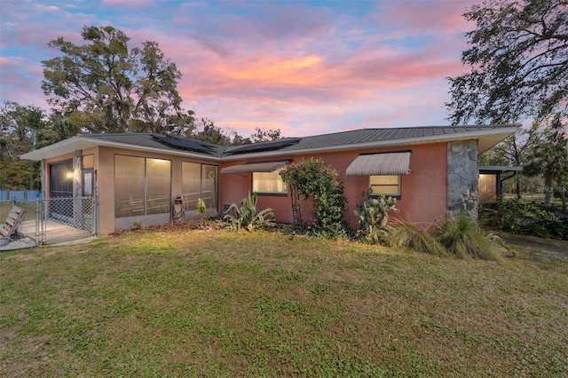 view of front of property featuring a gate, a sunroom, a front lawn, roof mounted solar panels, and metal roof