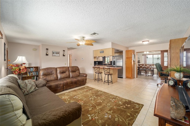 living room featuring ceiling fan, light tile patterned flooring, visible vents, and a textured ceiling