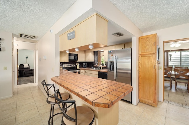 kitchen with a breakfast bar, black appliances, tile countertops, and visible vents