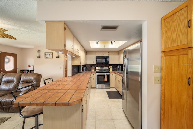 kitchen featuring visible vents, open floor plan, tile countertops, stainless steel appliances, and a peninsula