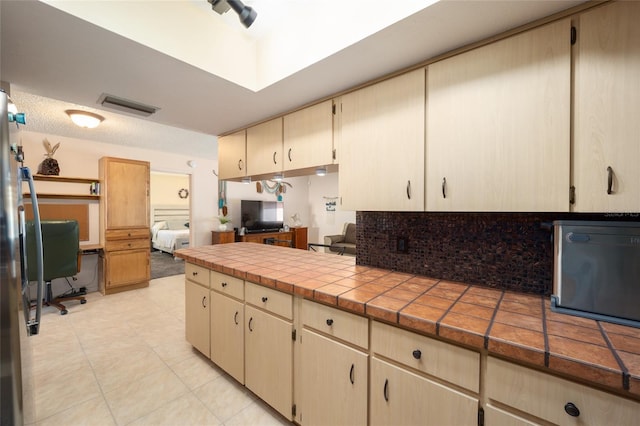 kitchen featuring visible vents, a peninsula, light tile patterned flooring, decorative backsplash, and tile counters