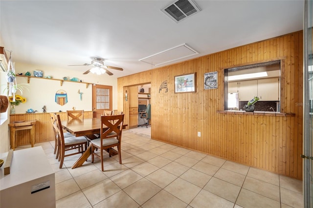 dining space with visible vents, attic access, light tile patterned flooring, ceiling fan, and wood walls