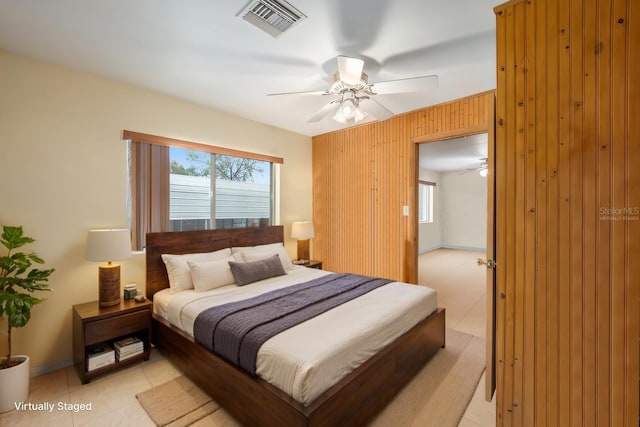 bedroom featuring visible vents, a ceiling fan, wood walls, light tile patterned floors, and baseboards