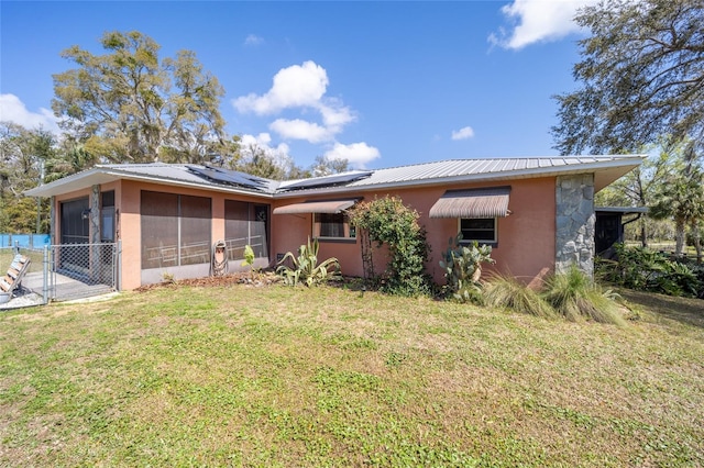 back of house featuring a lawn, a gate, roof mounted solar panels, a sunroom, and metal roof