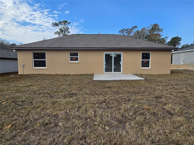 rear view of property with stucco siding, a lawn, roof with shingles, and a patio area