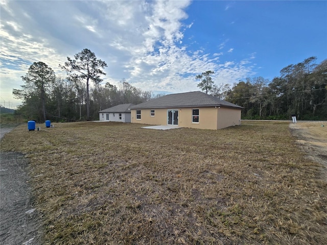 back of property with a patio area, stucco siding, and a yard