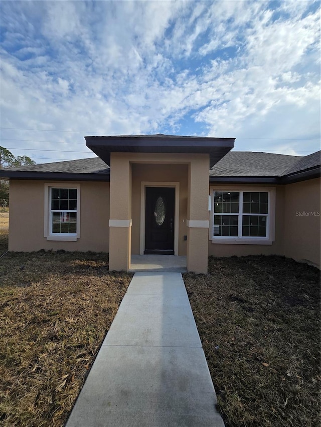 view of exterior entry featuring stucco siding and a shingled roof