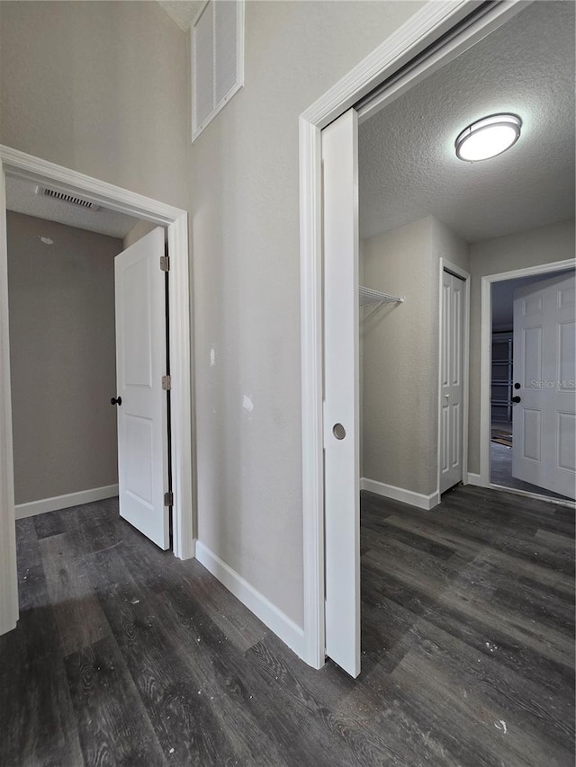 hallway with visible vents, a textured ceiling, baseboards, and wood finished floors