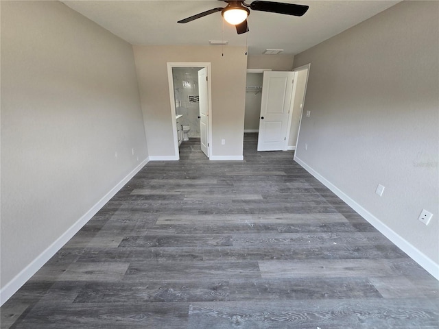 unfurnished bedroom with a walk in closet, ensuite bathroom, baseboards, and dark wood-style flooring