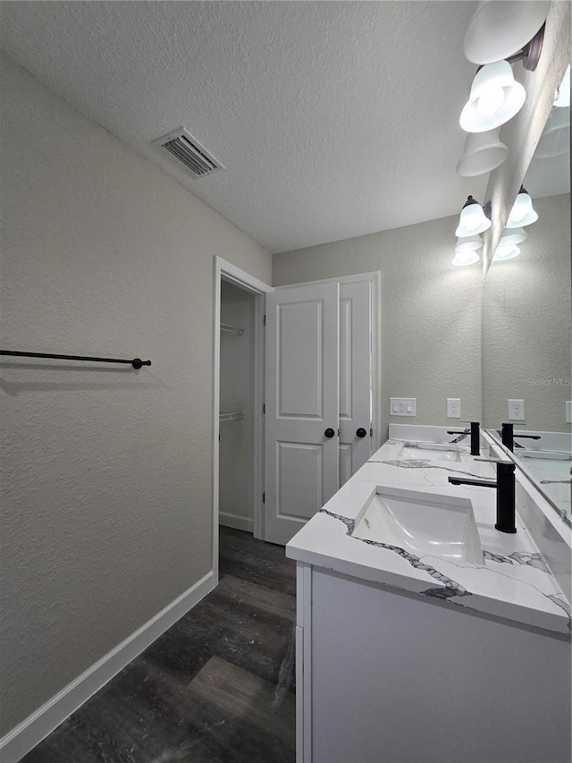 bathroom featuring baseboards, visible vents, a sink, a textured ceiling, and a textured wall