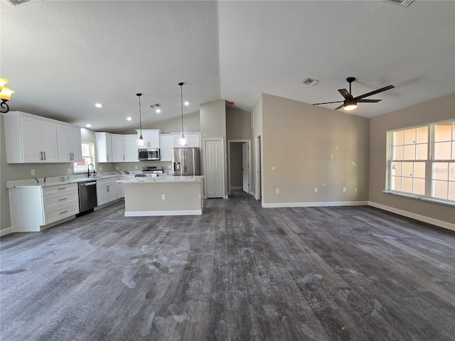 kitchen with a kitchen island, open floor plan, stainless steel appliances, white cabinets, and lofted ceiling