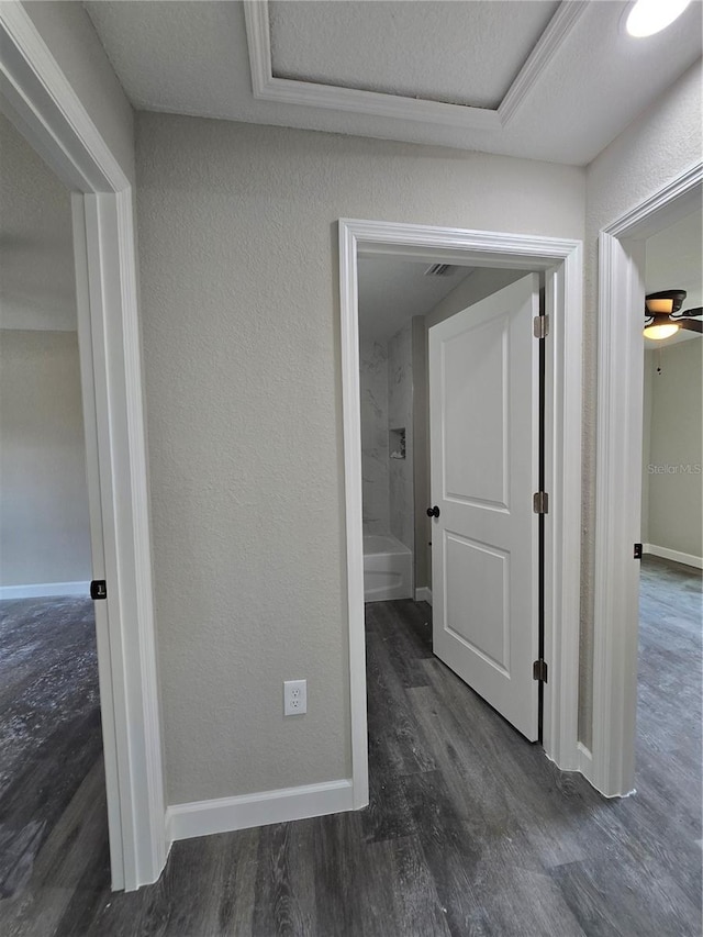 hall with a textured ceiling, baseboards, a textured wall, and wood finished floors