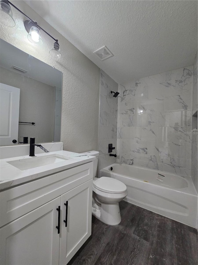 bathroom with wood finished floors, visible vents, a textured ceiling, toilet, and a textured wall