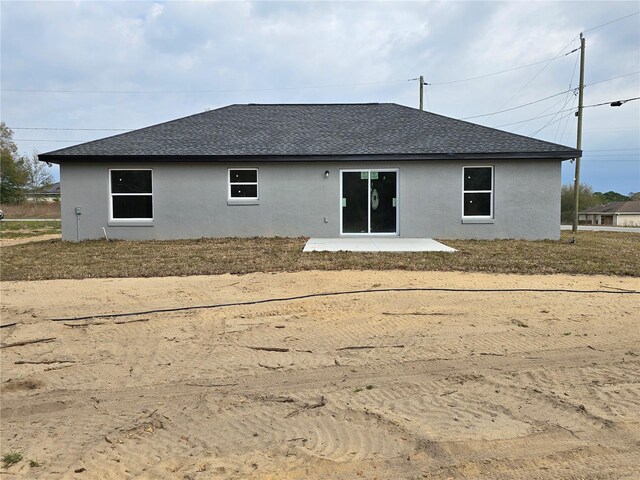 rear view of property featuring stucco siding, a shingled roof, and a patio