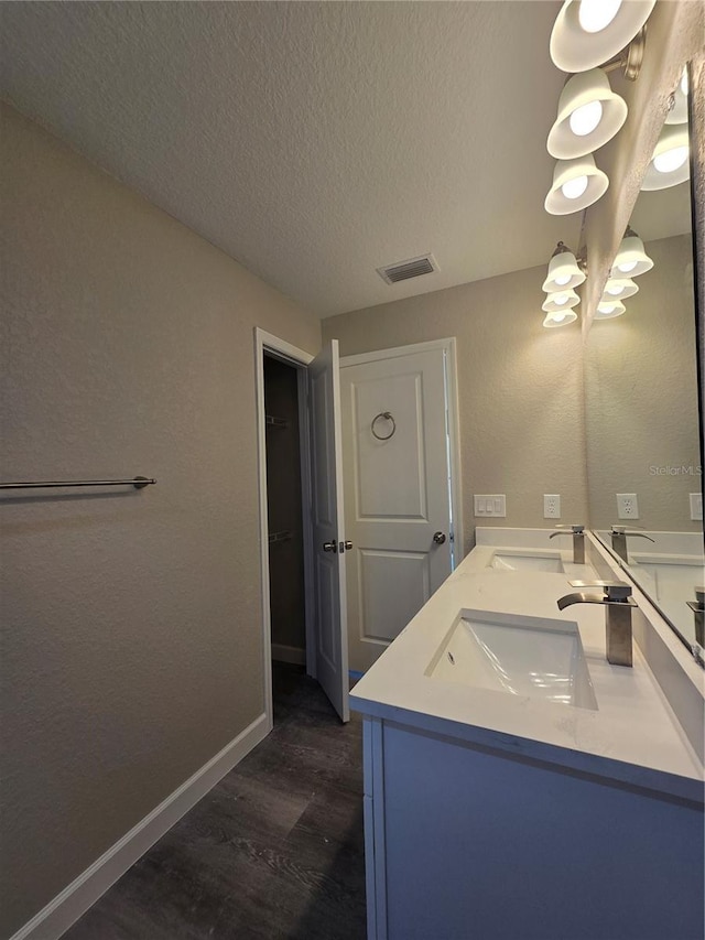 bathroom featuring baseboards, double vanity, wood finished floors, a textured ceiling, and a sink