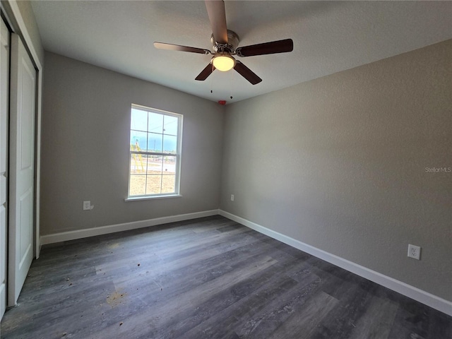 unfurnished bedroom featuring a closet, a ceiling fan, dark wood-type flooring, and baseboards