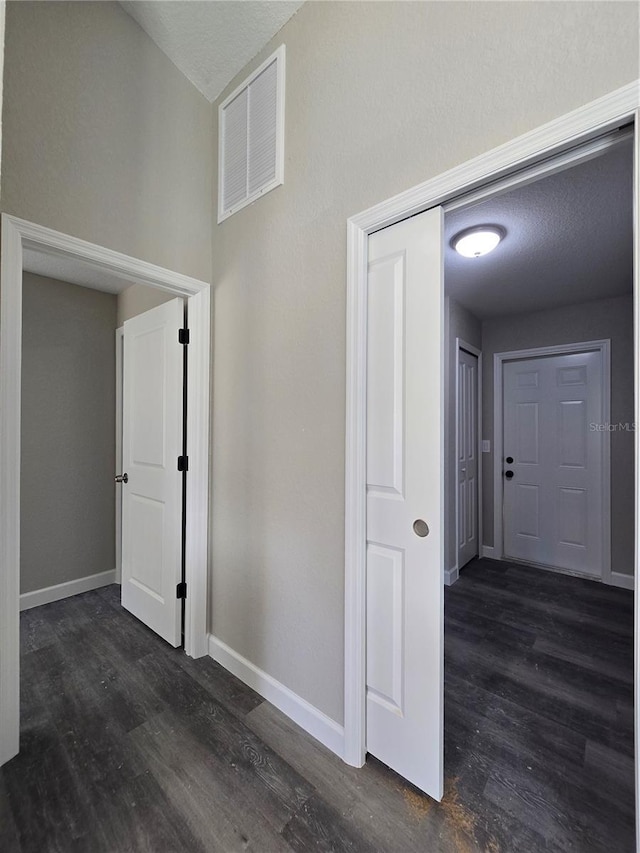 corridor featuring visible vents, baseboards, a textured ceiling, and dark wood-style floors