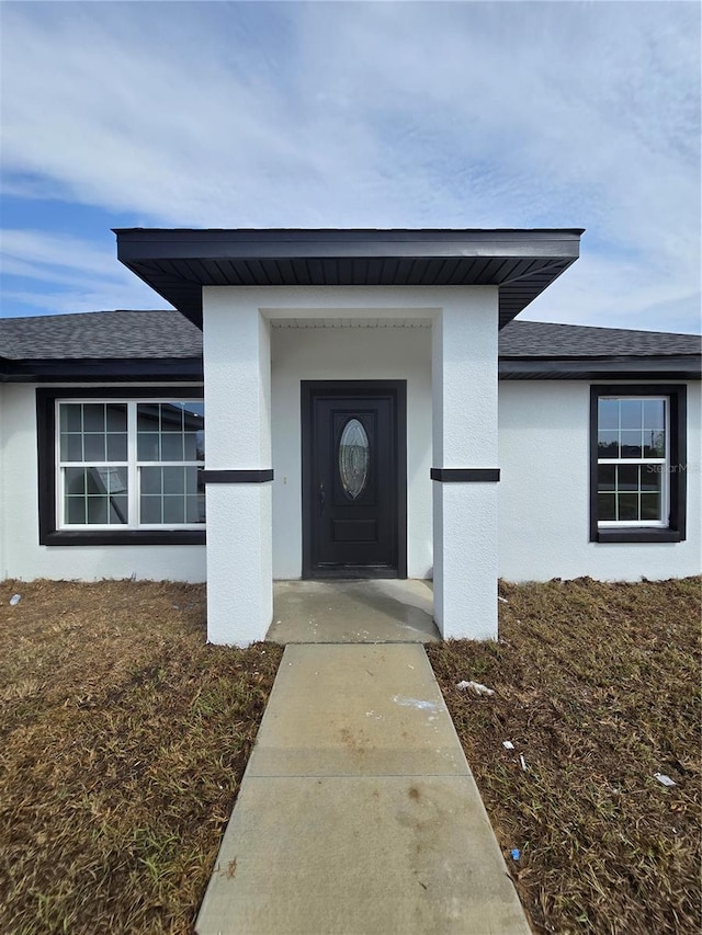 doorway to property with stucco siding and a shingled roof