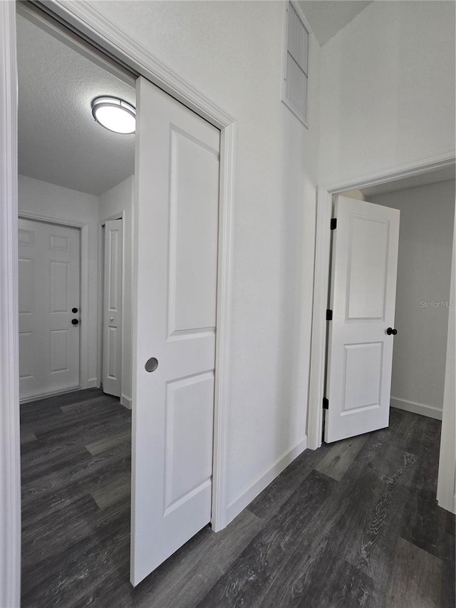 hallway featuring visible vents, baseboards, dark wood-style flooring, and a textured ceiling