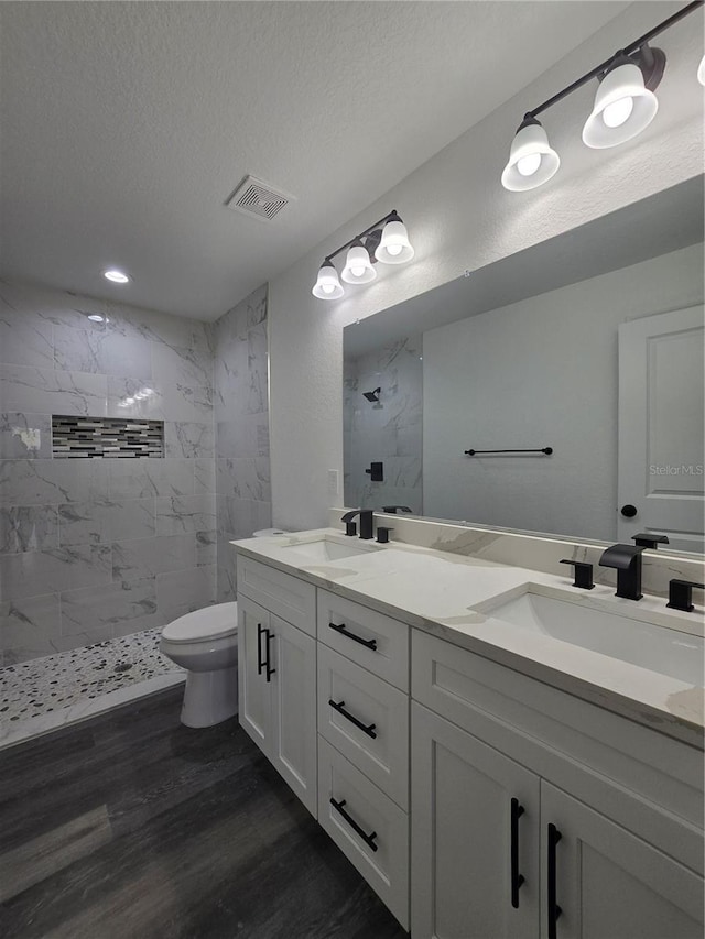 bathroom with wood finished floors, tiled shower, double vanity, and a sink