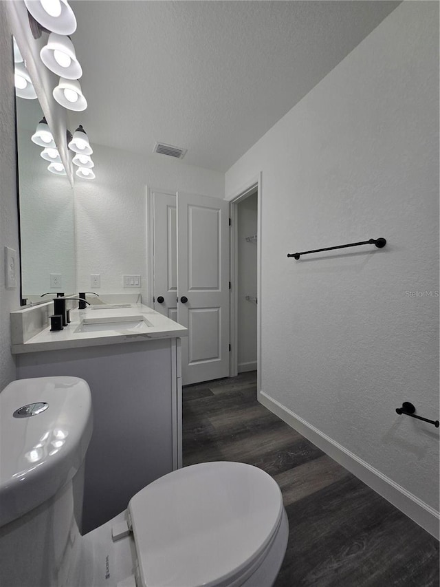 bathroom with wood finished floors, baseboards, visible vents, a textured ceiling, and a textured wall