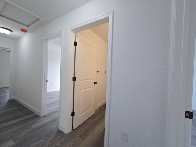 hall with attic access, baseboards, and dark wood-style flooring