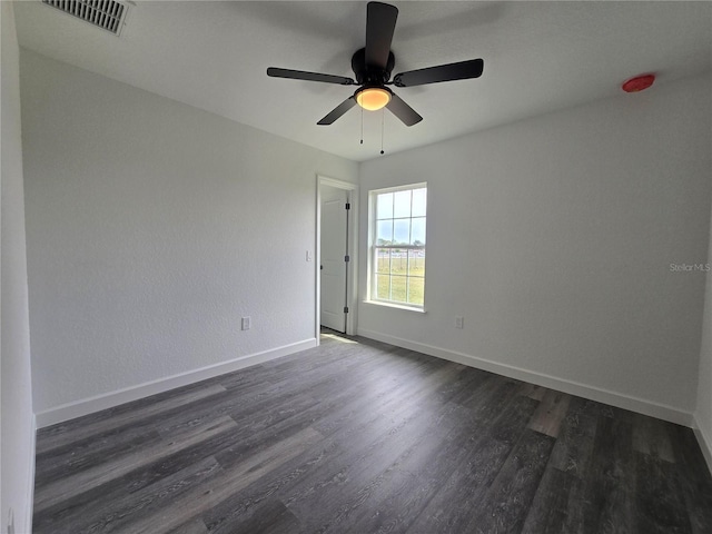 unfurnished room with a ceiling fan, dark wood-style floors, visible vents, and baseboards