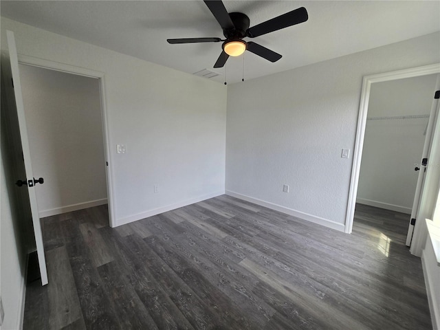 unfurnished bedroom with a closet, baseboards, dark wood-style floors, and a spacious closet