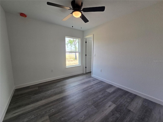 spare room featuring a ceiling fan, dark wood-style floors, and baseboards