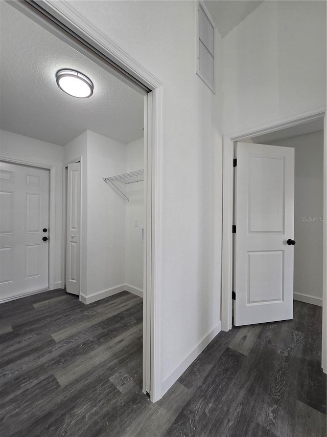 corridor featuring a textured ceiling, baseboards, and dark wood-style flooring