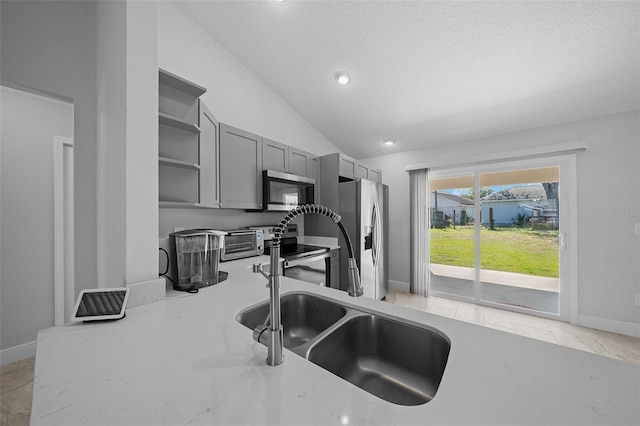 kitchen with open shelves, lofted ceiling, gray cabinetry, stainless steel appliances, and a sink