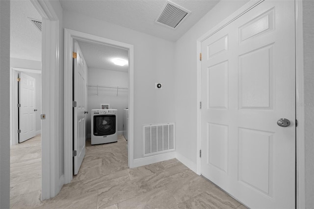 hall with visible vents, washer / dryer, a textured ceiling, and baseboards